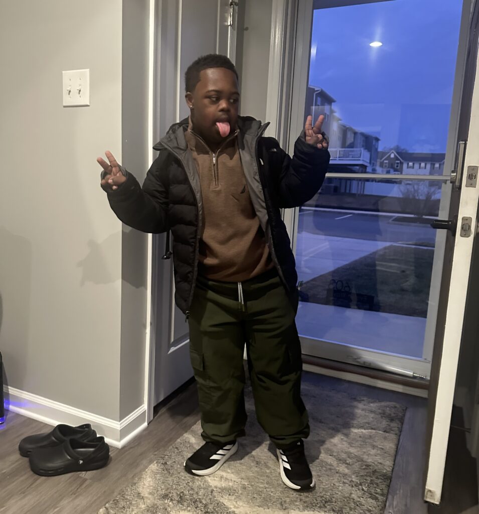 Bryan poses for a photo in the entrance to his home with his tongue out and holding up 2 fingers in both hands.