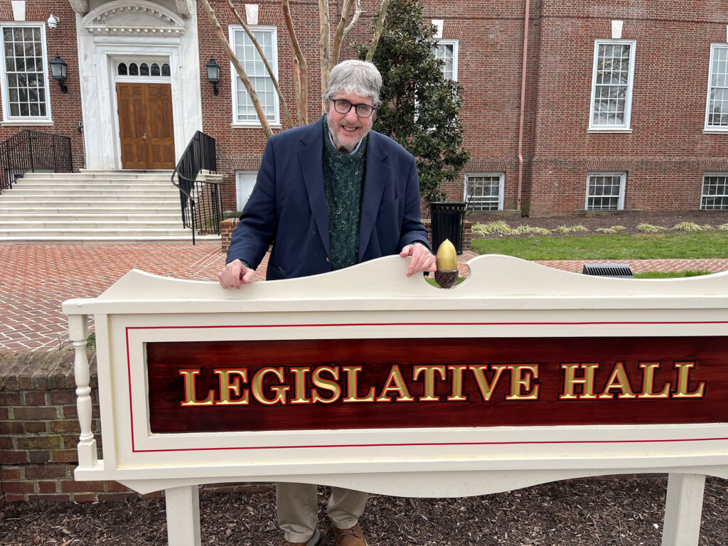 John Flaherty is posing for a photo behind the sign for Legislative Hall.