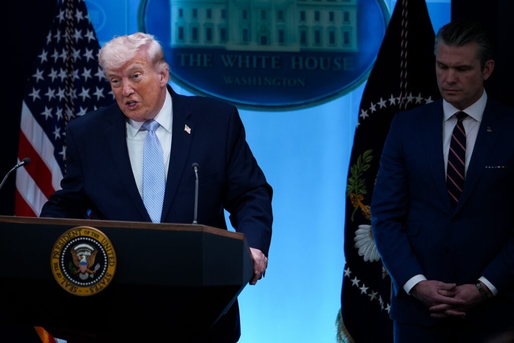 Trump Donald Trump speaking at a podium, with Pete Hegseth standing beside him.