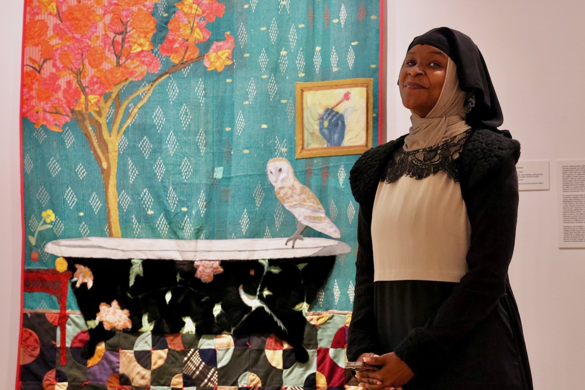 December Collins poses for photo in front of quilts at the Fabric Workshop exhibit