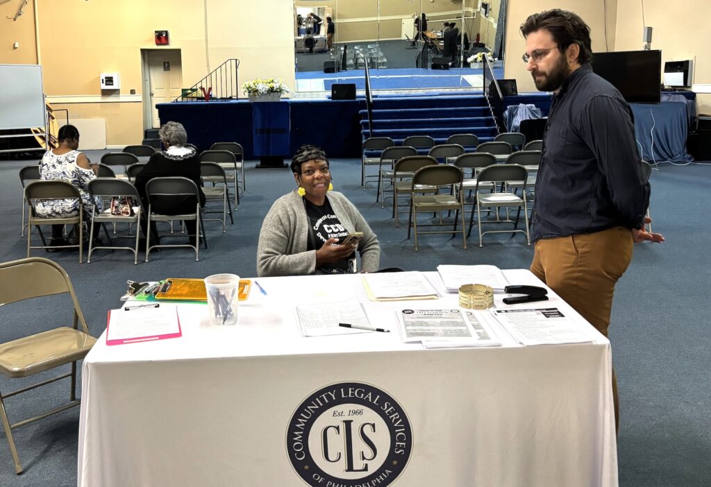 Two people who are representatives from Community Legal Services are stationed behind the table at the entrance of the room.