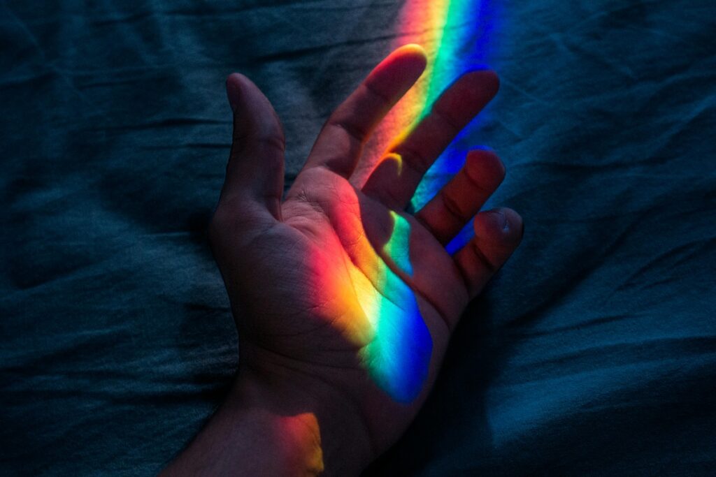 pexels-barcelos_fotos-1484908-3121976 An open palm hand with four colored light shinning on it —red, yellow, green and blue.