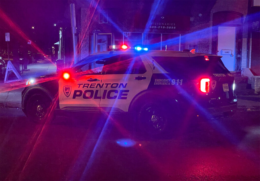 A Trenton Police car is parked in the street at night with it's siren flashing