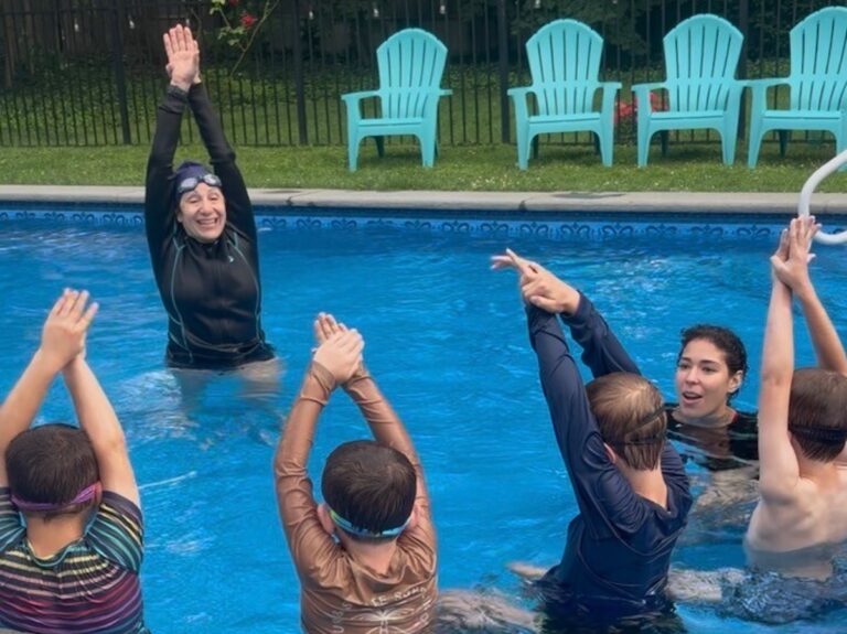 Jennifer May is teaching a swimming lesson in the pool to children.