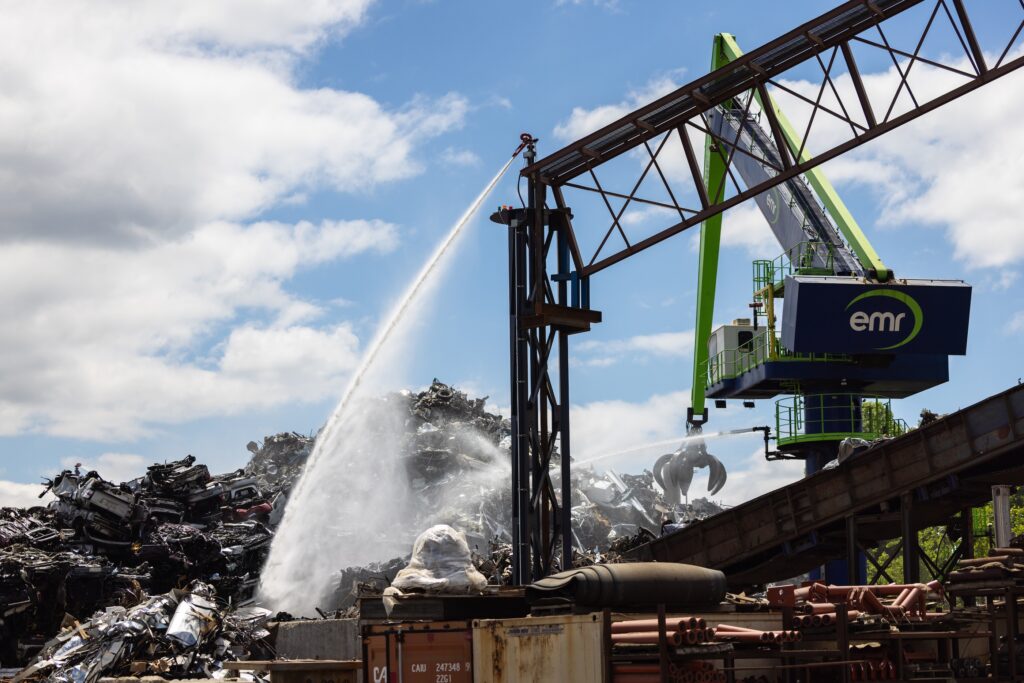 A large crane shoots water down at a pile of scrap metal.