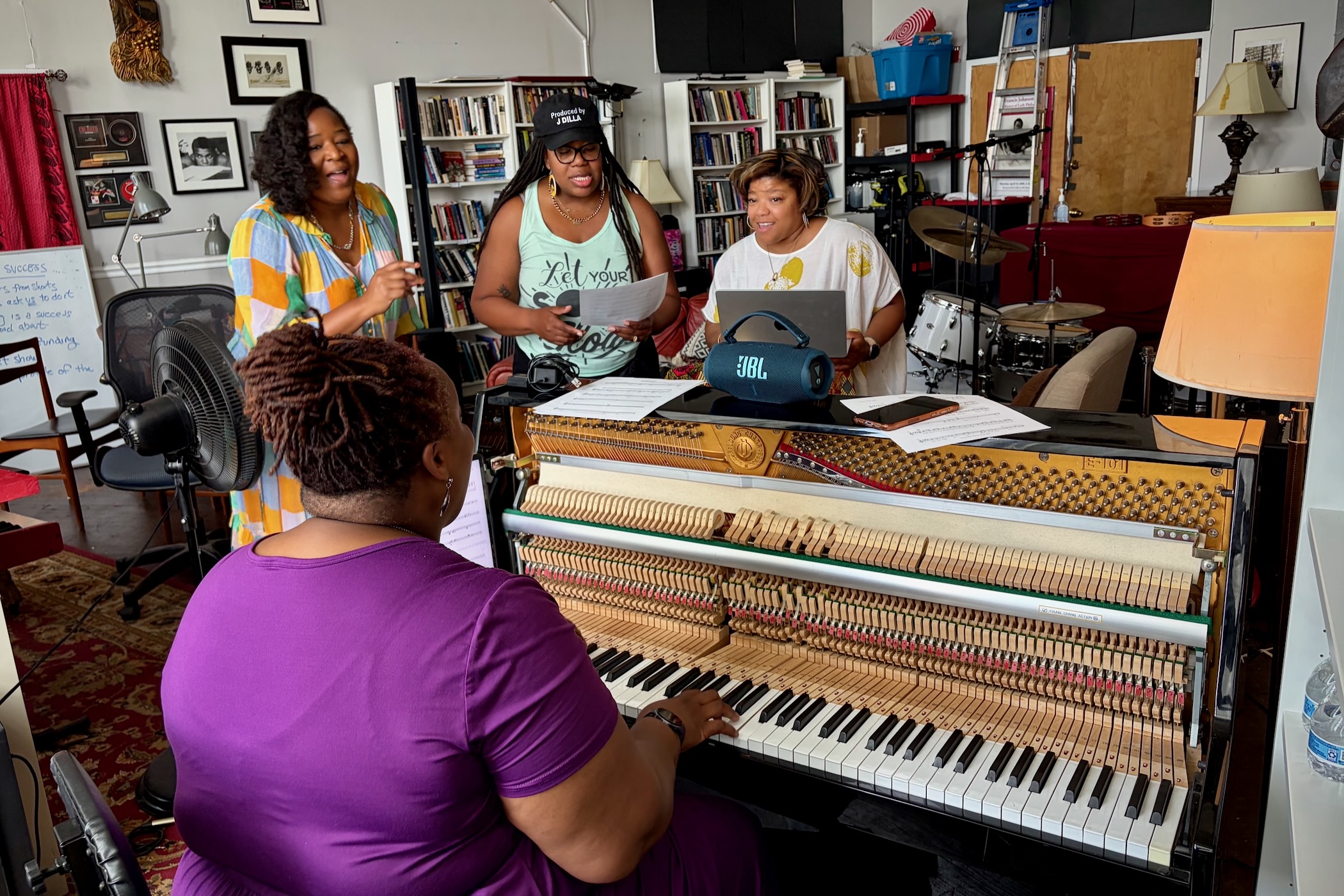 Kendrah Butler-Waters is playing the piano, while a group of singers are rehearsing with her.