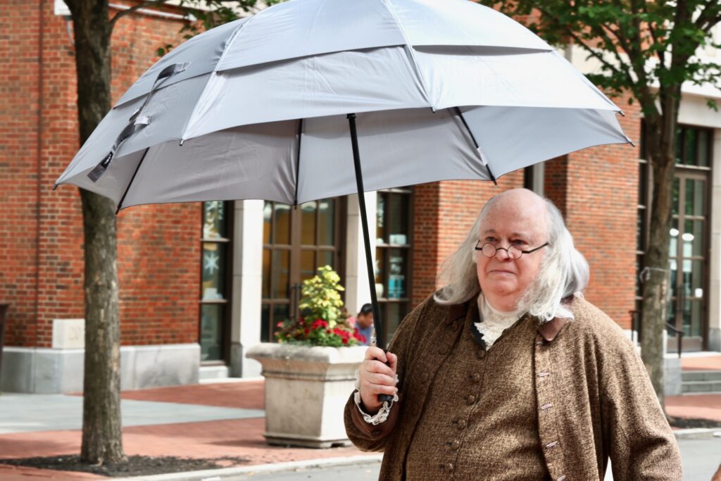 A Benjamin Franklin impersonator uses an umbrella to stay out of the sun in Philadelphia's Old City neighborhood on Tuesday, June 30, 2026.