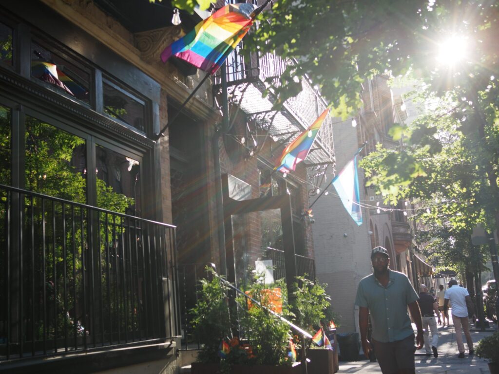 Pride flags hang from apartment buildings on a city street.