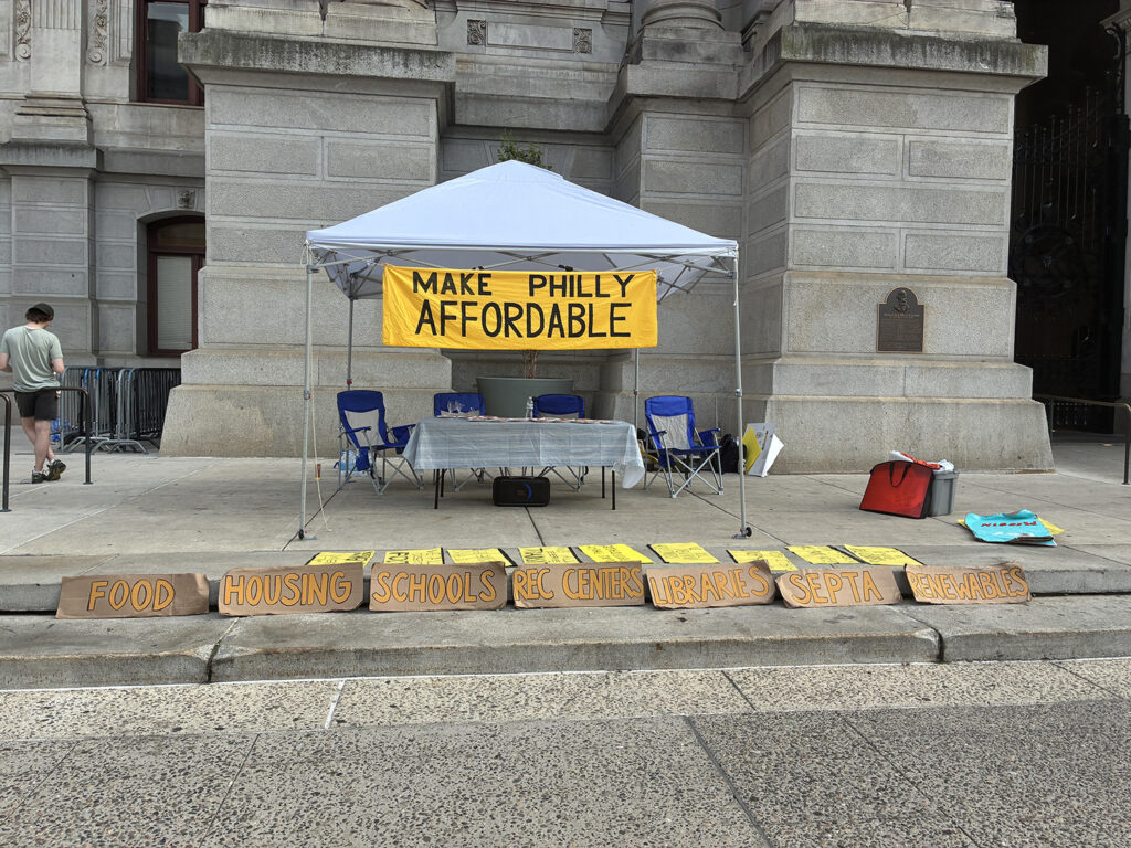 A banner hung up on Sunrise Movement Philadelphia’s tent outside City Hall reads “Make Philly Affordable.”