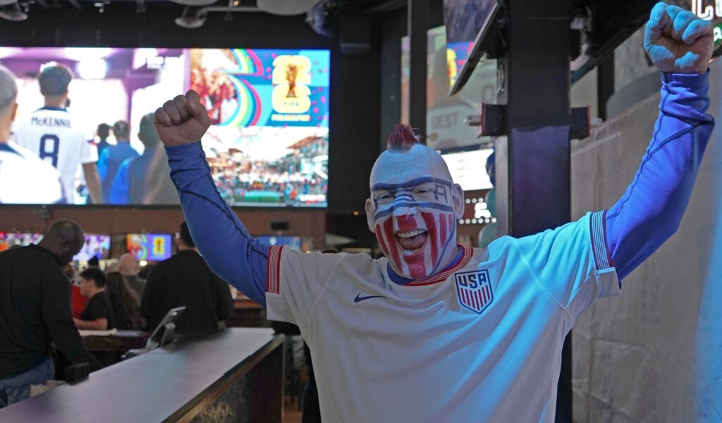 A man cheers in a bar with face paint of the American flag