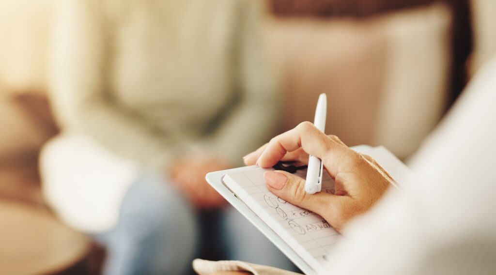 The hands of someone holding a pen and notepad while talking to someone else are seen.