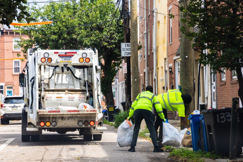 07 10 2026 k paynter trash collectiong truck and sanitation philadelphia Sanitation workers load bags of trash into the back of the truck.