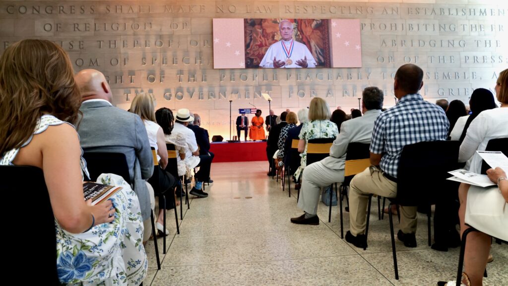 People in the audience at the National Constitution Center watch Pope Leo XIV's video remarks on a large screen.