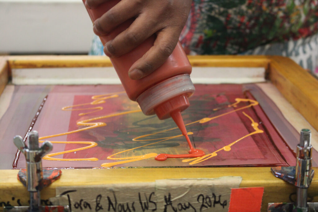 A hand squeezes paint through a bottle onto a canvas