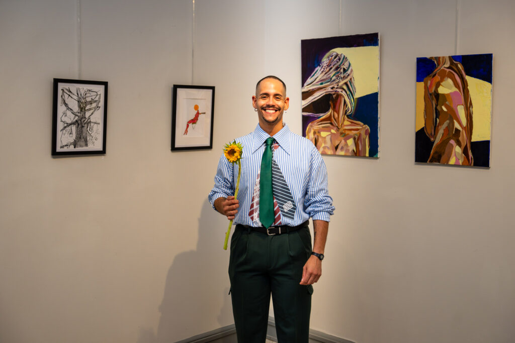 juan-santos-delaware-exhibition-becoming Dominican-born Delaware artist Juan Santos stands in front of his paintings holding a yellow flower