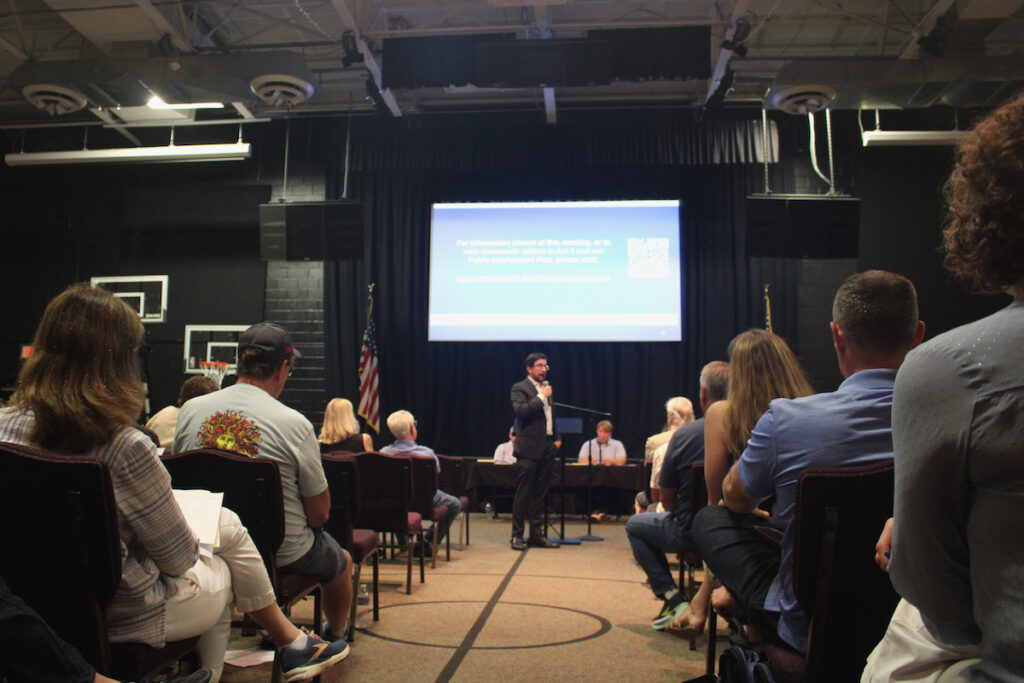 Ben Weldon is speaking into a microphone during the town hall meeting.