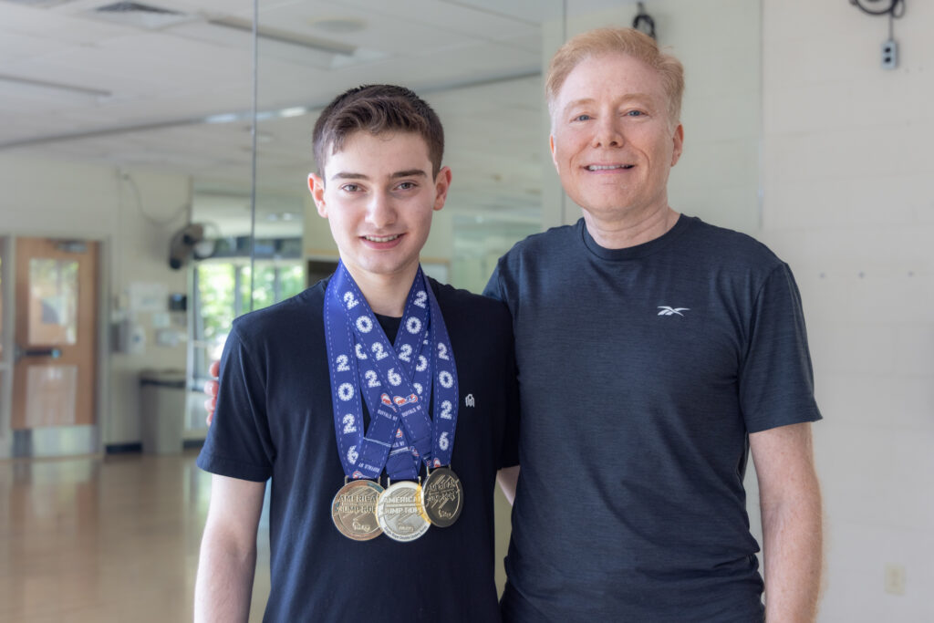 17-year-old Zach Peckman poses for a photo with his father Marcus in the YMCA. Zach has 3 medals hanging around his neck.