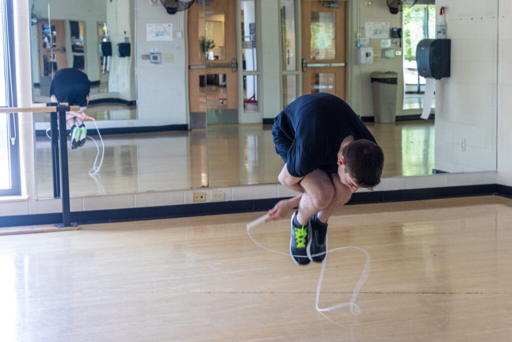 Zach Peckman is in mid-air as he is jumping rope. He is hunched far forward, with his arms beneath his legs as he does a trick with the rope inside the YMCA in Doylestown, Pa.