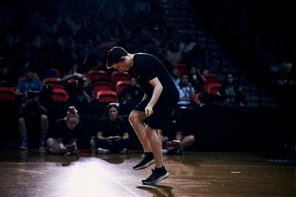 07 31 2026 k paynter jump rope champ-4 Zach Peckman is jumping rope at the competition in Buffalo, NY. He is hunched forward and is whipping the rope so quickly it is barely visible. A crowd of onlookers watch.
