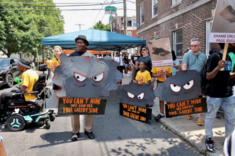 Protesters march outside Avondale Apartments with signs reading YOU CAN'T HIDE WE CAN SEE YOUR GREEDY SIDE