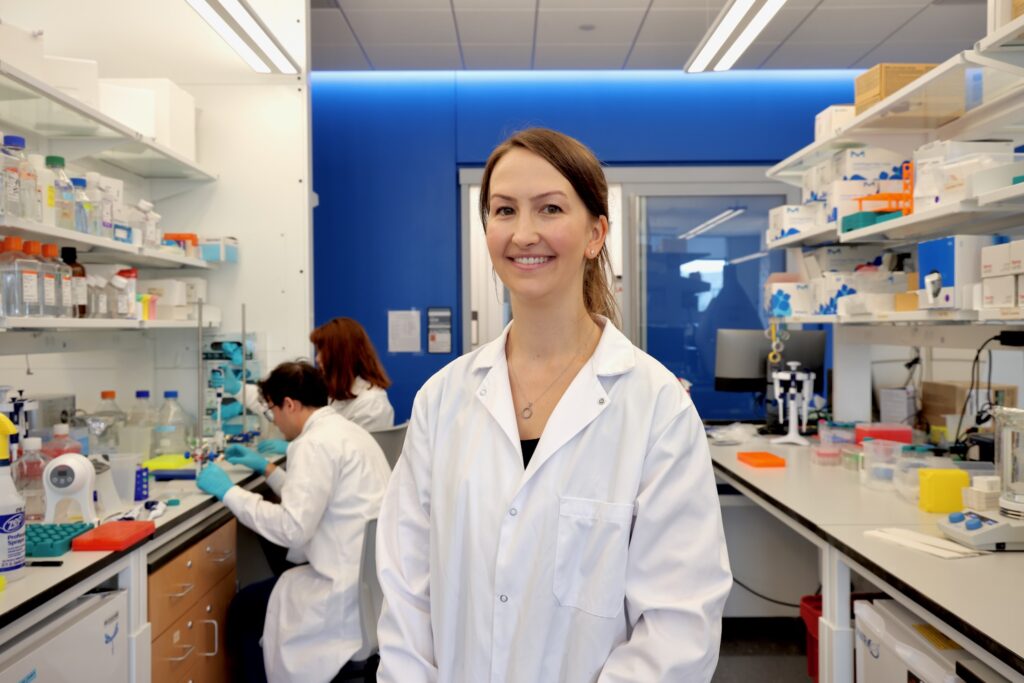 2026 07 30-e lee-brittney allyn-philadelphia university of pennsylvania-mrna research celiac Brittney Allyn is in her busy lab at University of Pennsylvania. Two researchers are working together at at table behind her.