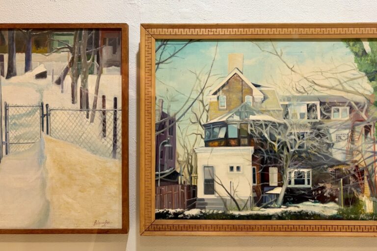 Two paintings by Rebecca Rose Metzger on a wall. They show a snowy gate and a home