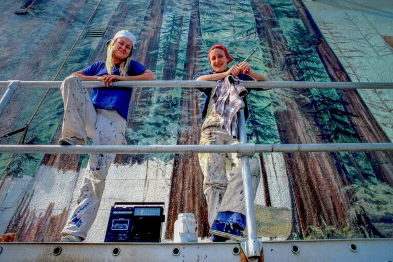 Jane Golden and an assistant smile while working on a mural