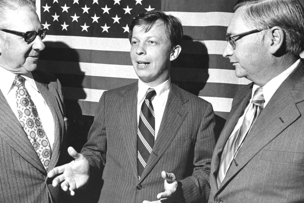 Franklin-Kury-PaHouseArchives-1 Franklin Kury speaking with 2 other men while standing in front of a large American flag.