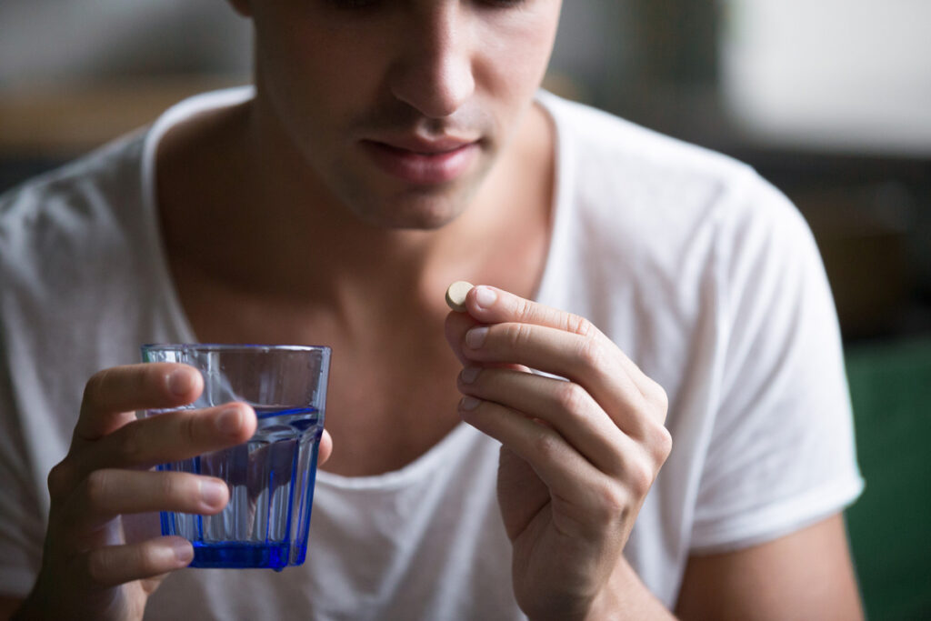 Sick Ill Depressed Man Holding Glass Of Water Taking Pill Suffer A person prepares to take a medication while holding a glass of qater
