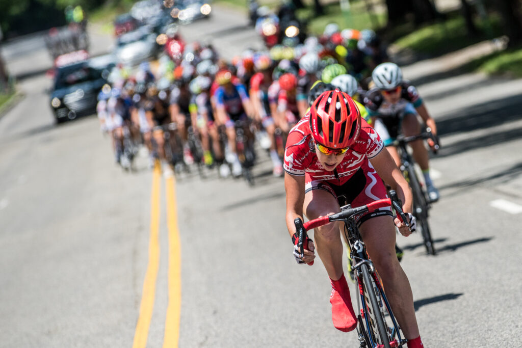 a competitor rides her bicycle in front of other cycling competitors along a road