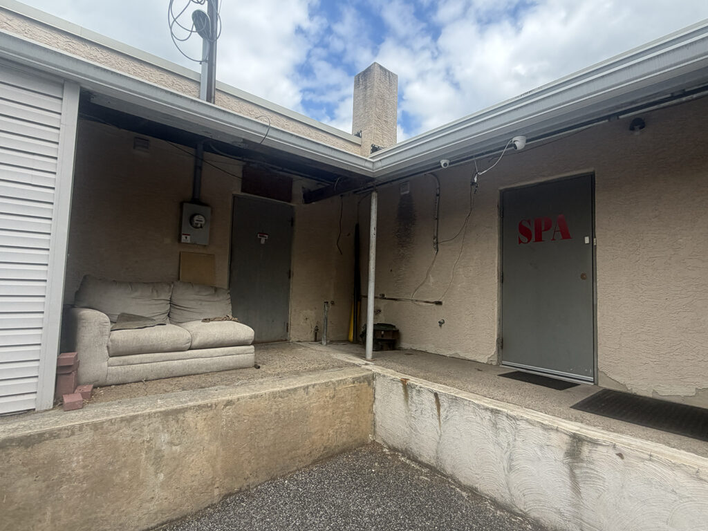 A couch sits outside of a business where two cameras sit above a door with the word "SPA" on it in red letters