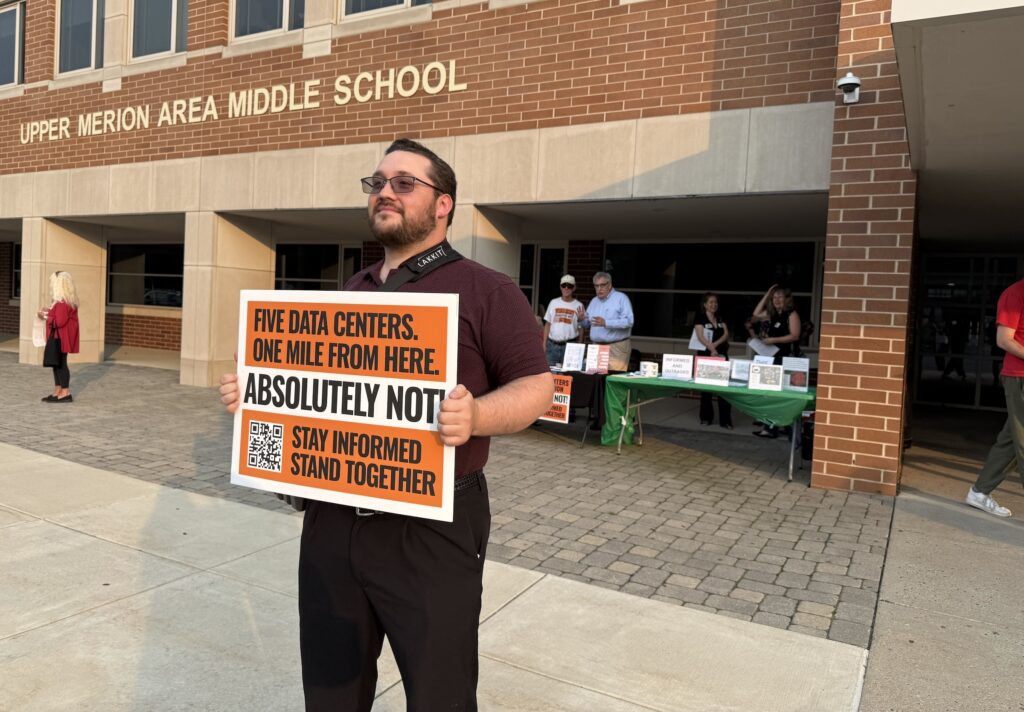data-center-meeting-zread-2026-08-14-1 A man holds up a sign protesting against data centers outside of the middle school.