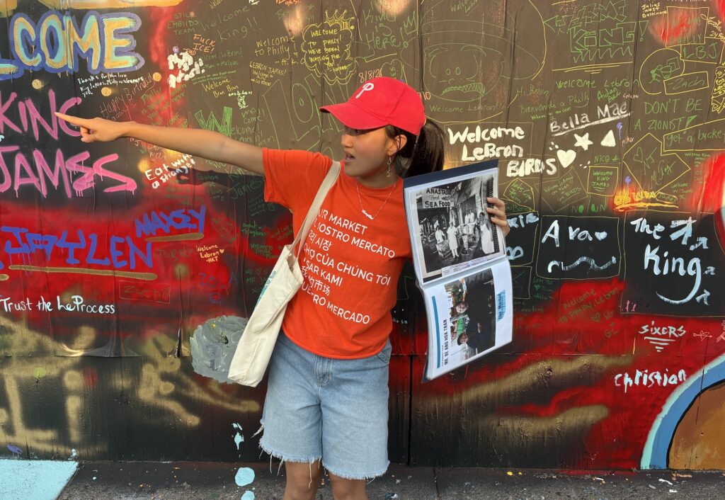 Melissa Yong is holding up a historical photograph as she points out locations during a tour of the Italian Market.
