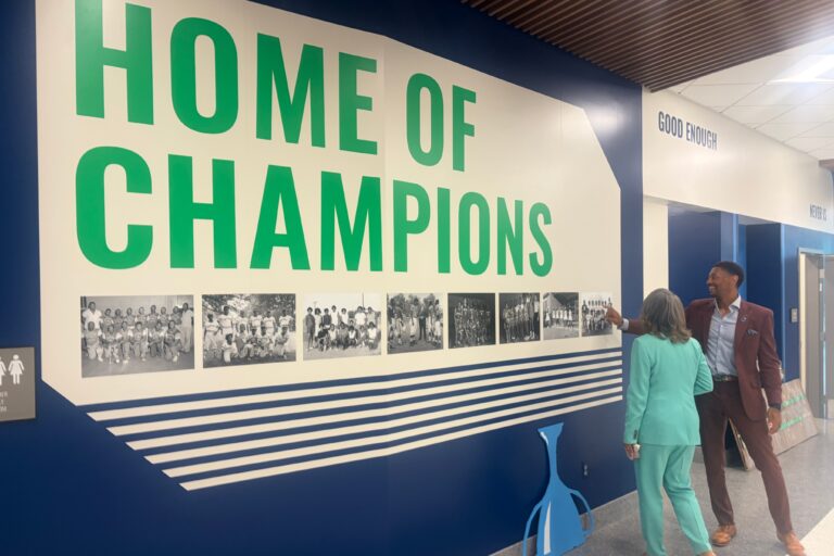 Logan Herring and Lisa Blunt Rochester look at a wall that reads HOME OF CHAMPIONS