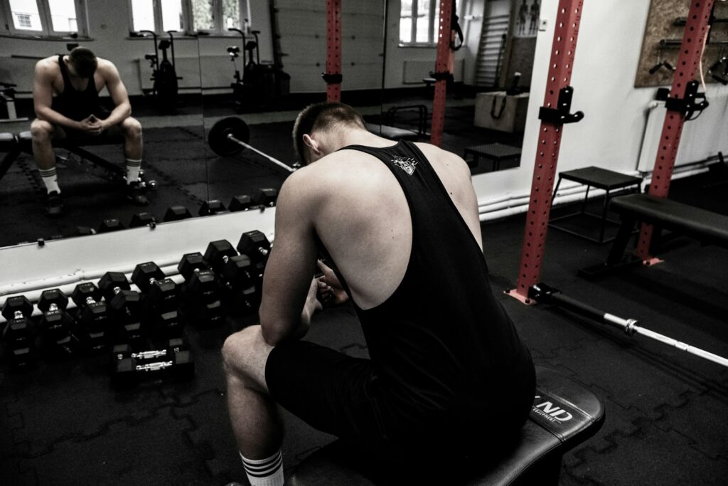 maciej-karon-M4rhdJkvAqQ-unsplash a man sits hunched over in a gym