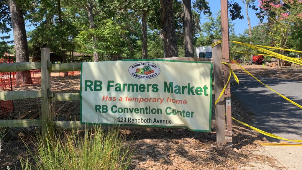 rehoboth-beach-farmers-market-2026-sg-2 a sign reads Rehoboth Beach Farmers' Market Has a temporary home RB Convention Center 229 Rehoboth Avenue