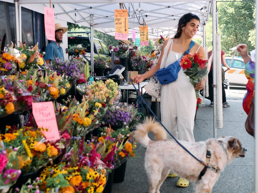 westphilly-summer-farmer-market A woman shops for flowers at a farmers market with her dog.
