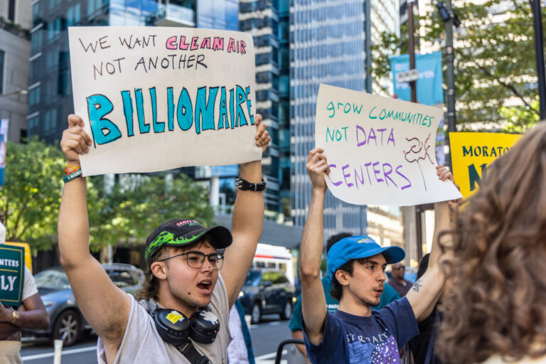 two people hold signs reading WE WANT CLEAN AIR NOT ANOTHER BILLIONAIRE and GROW COMMUNITIES NOT DATA CENTERS in Philadelphia