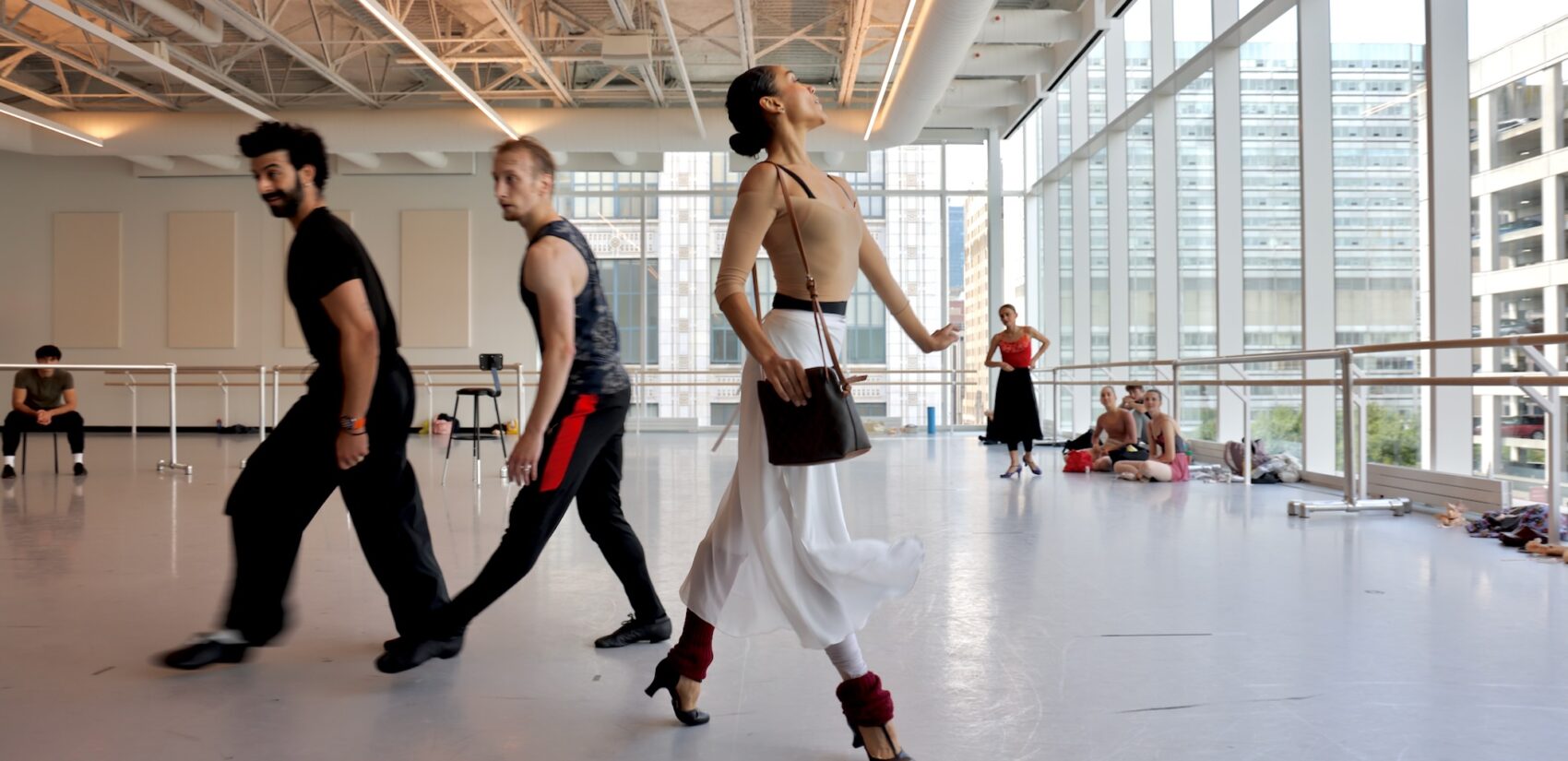 In a large open room, many ballet dancers are rehearsing.
