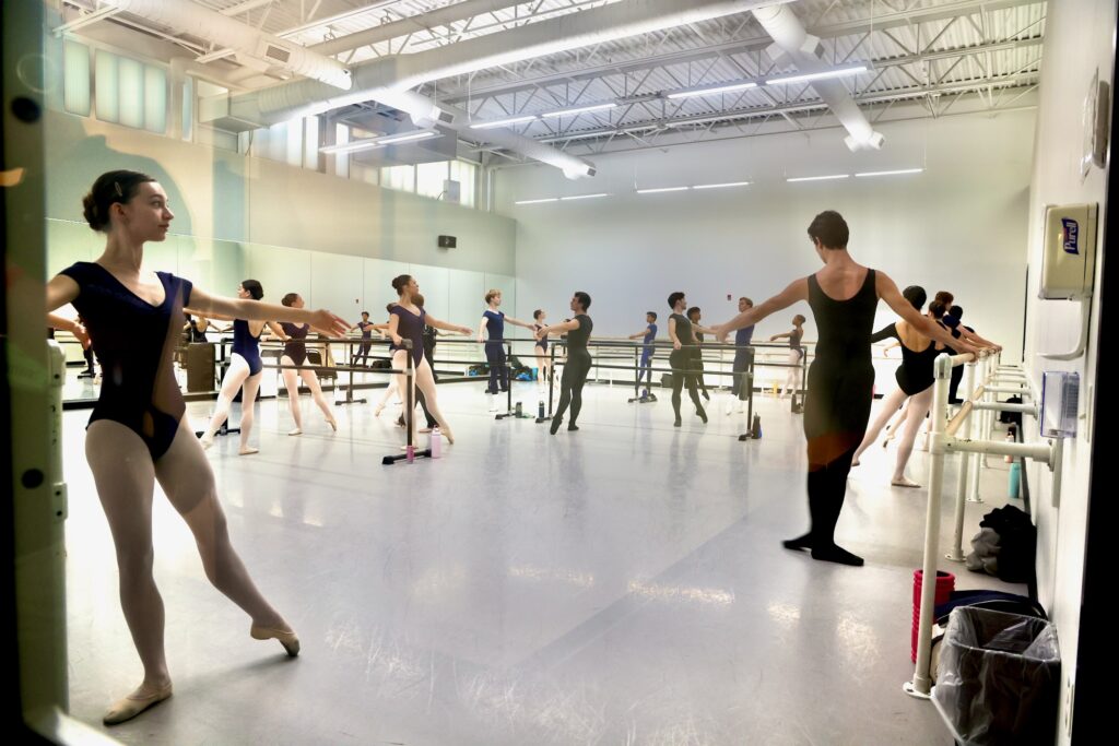 2026 09 03-e lee-philadelphia ballet-new building sneak peak school studio reflections In a large open classroom at Philadelphia Ballet, many ballet dancers are rehearsing.
