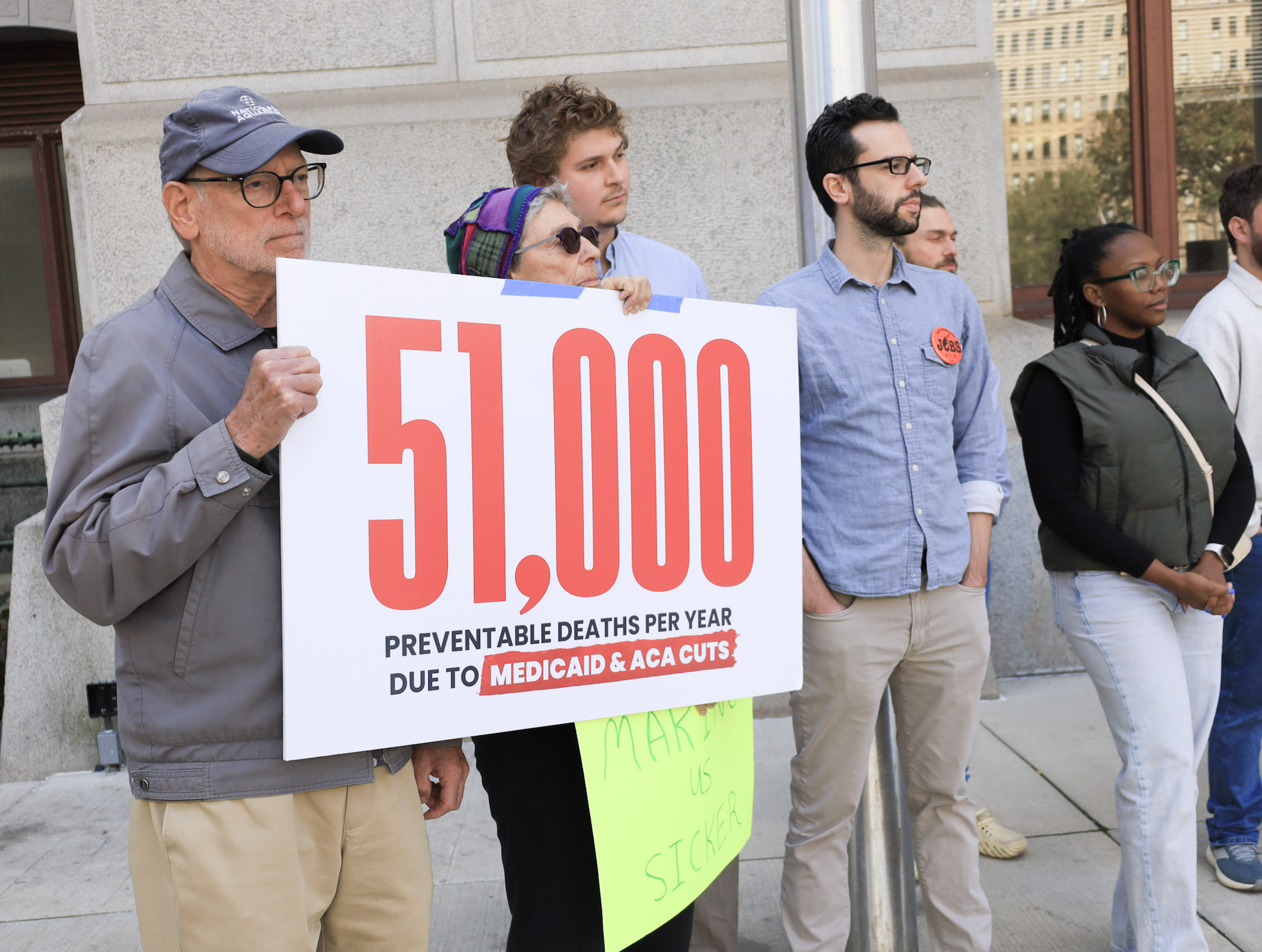 rallgoers by a sign reading 51,000 PREVENTABLE DEATHS PER YEAR DUE TO MEDICAID & ACA CUTS