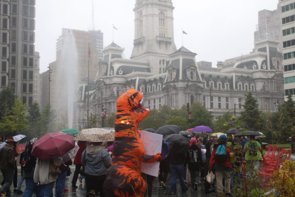 academy-sciences-supporters-bp-092826 Marchers under umbrellas and dinosaur costumes