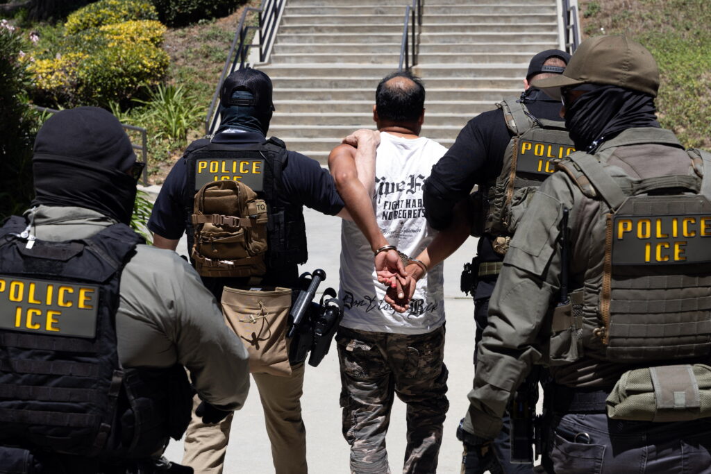 GettyImages-2287296268.jpg Four Immigration and Customs Enforcement agents walk a detainee out of the Ventura County Government Center in Ventura, California, on July 27. The individuals are photographed with their backs to the camera, and the detainee is handcuffed behind his back. The agents are wearing bulletproof vests that say