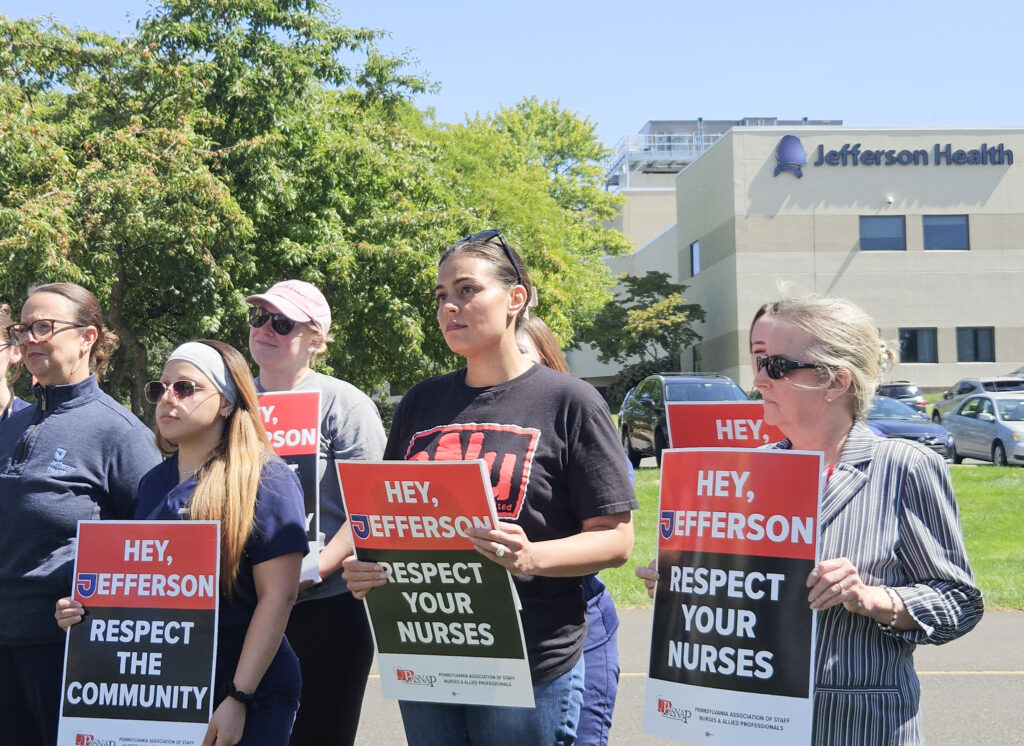 jefferson-health-unionize-2026-09-08-nl-1 Jefferson Health registered nurses hold signs reading HEY, JEFFERSON RESPECT THE COMMUNITY and HEY, JEFFERSON RESPECT YOUR NURSES