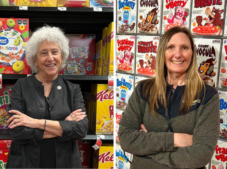Marion Nestle and Lisa Sutherland stand in front of dozens of cereal boxes, stacked in a grocery aisle.