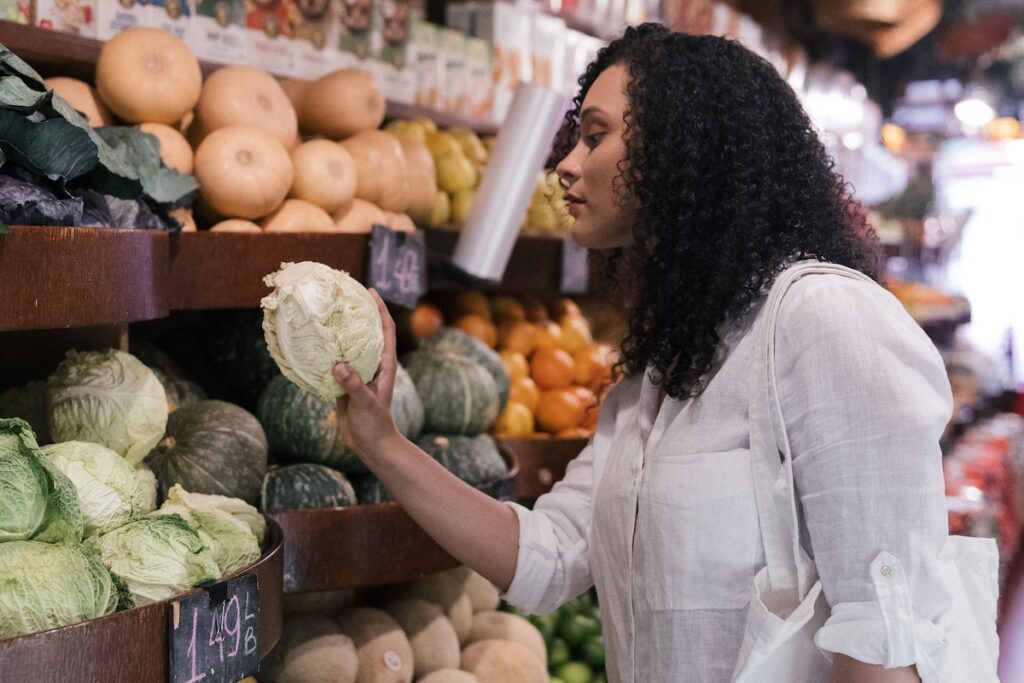 pexels-mike-jones-8805173 A woman in a white shirt picking out a cabbage in a grocery store.