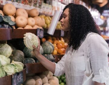 pexels-mike-jones-8805173 A woman in a white shirt picking out a cabbage in a grocery store.