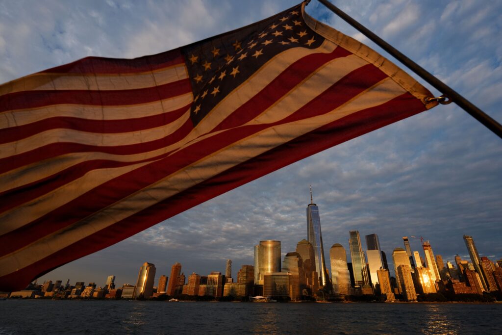 APTOPIX Sept 11 Tribute in Light Test In the foreground, an American flag waves in the air. The skyline of lower Manhattan in NYC is in the background.
