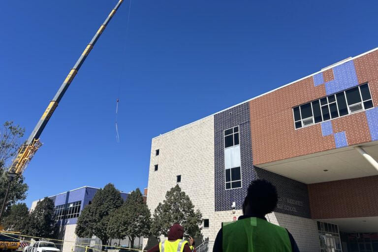 Students watching crane lift building materials