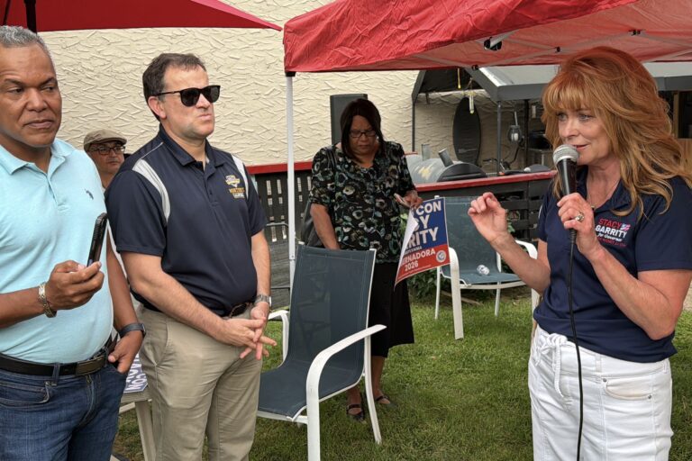 Stacy Garrity speaks while four people are seen listening